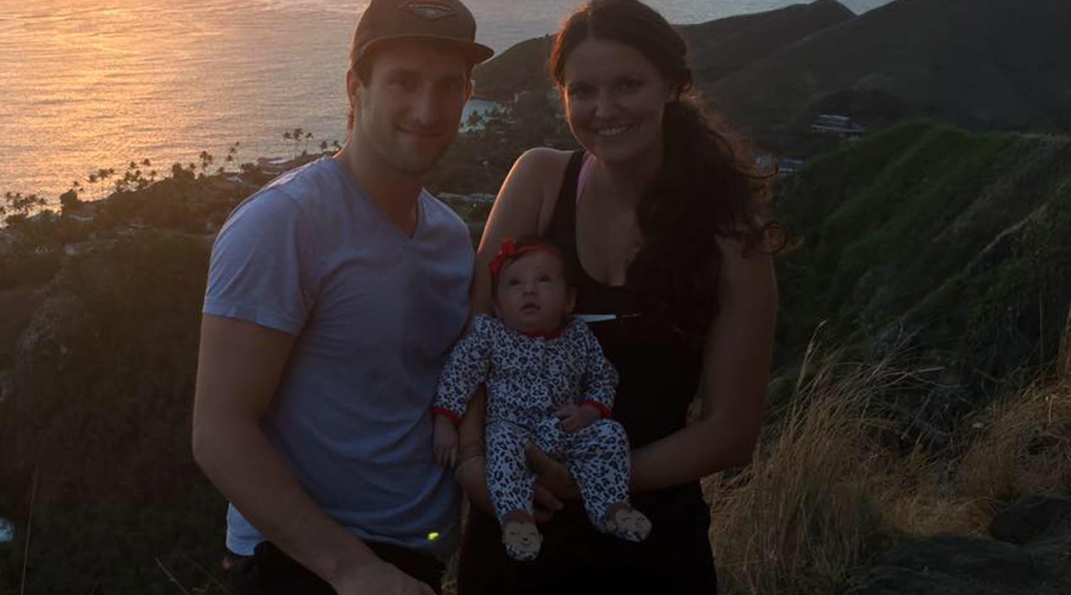 Hannah and Ben Hinders posing with their baby with the ocean in the background
