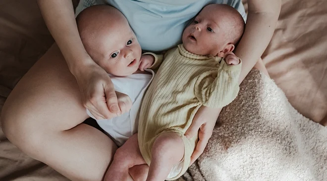 baby twins in mother's lap on bed