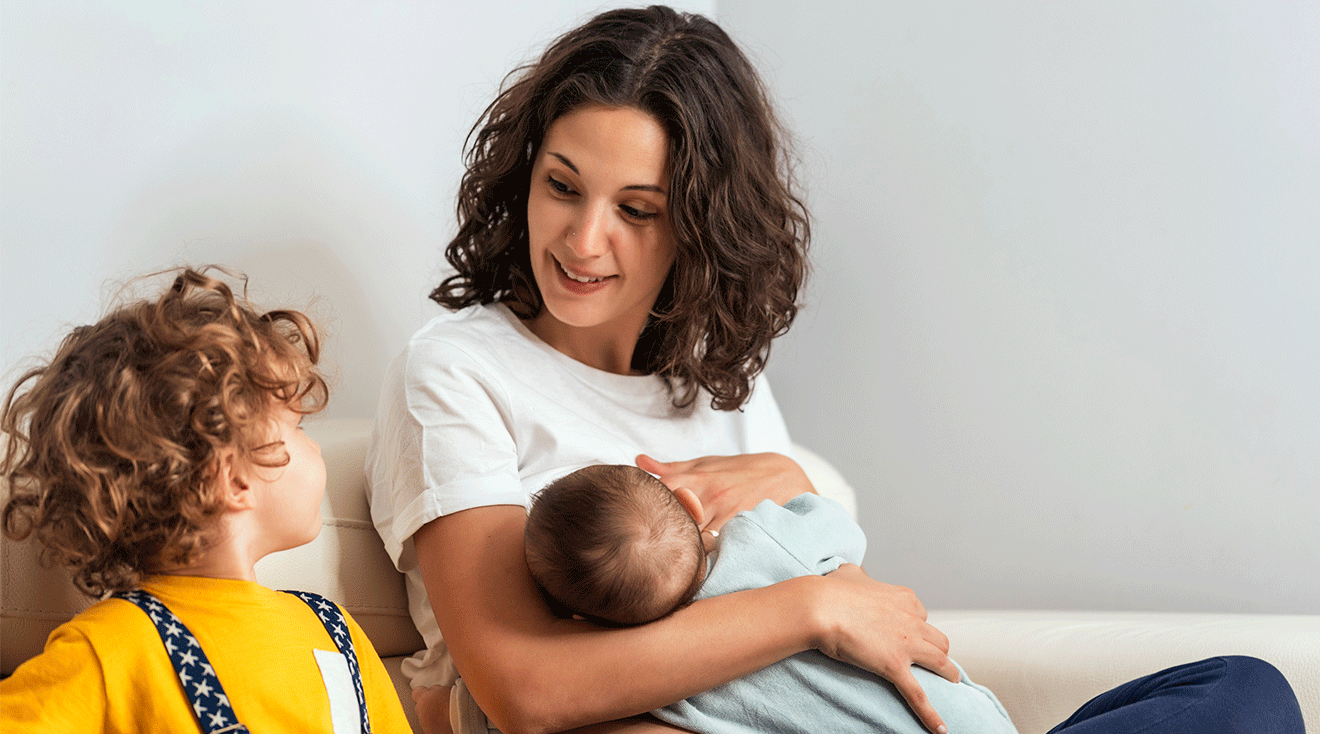 mom breastfeeding newborn baby while sitting next to toddler