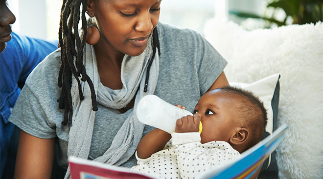 mom feeding her baby a bottle and reading him a book