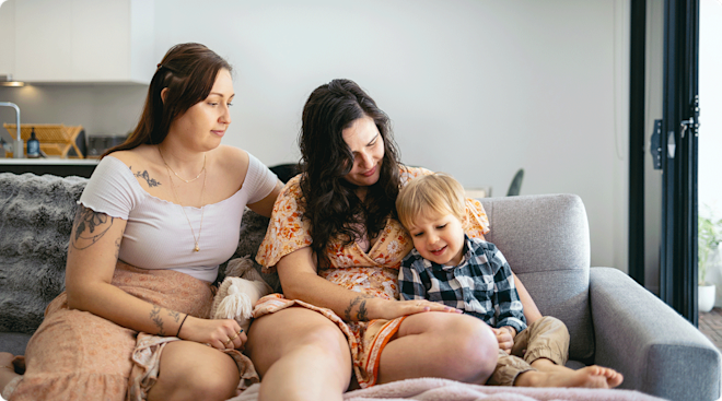 two moms sitting on the couch at home with toddler