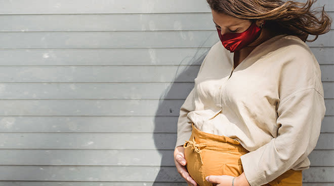 Pregnant woman outside wearing a mask and holding her belly. 