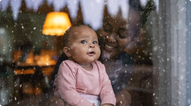 mom and baby watching snow fall outside window