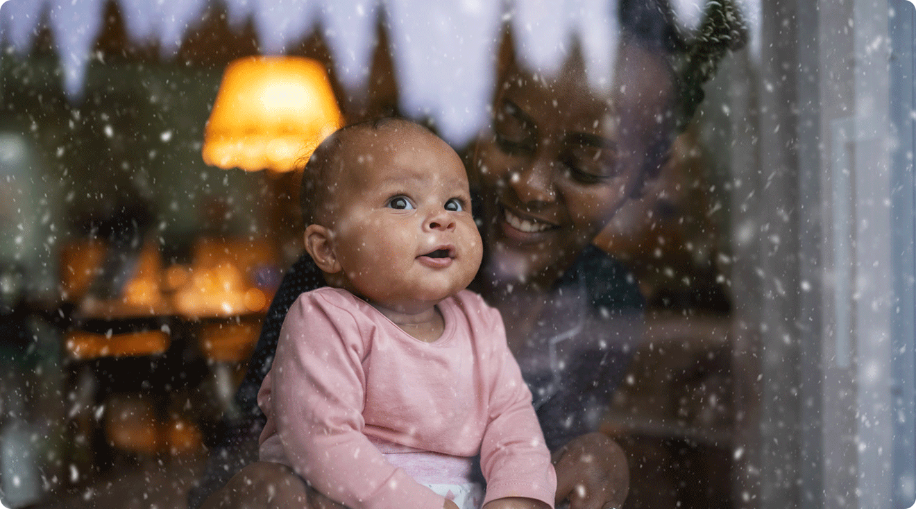 mom and baby watching snow fall outside window