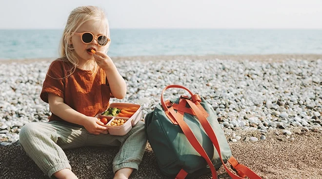 young girl wearing sunglasses and eating healthy snacks by the beach