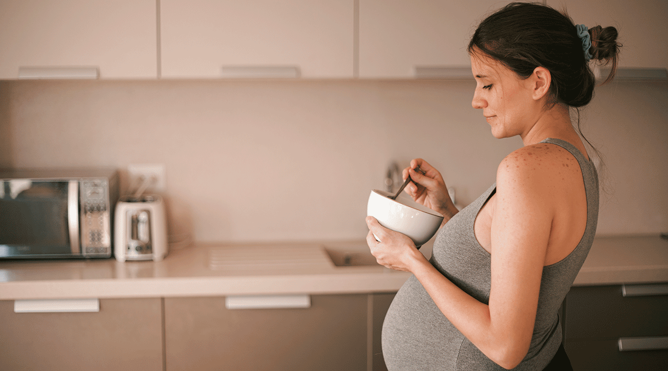 pregnant woman eating out of a bowl in kitchen