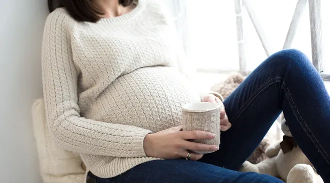 pregnant woman wearing a sweater and holding a cup of tea