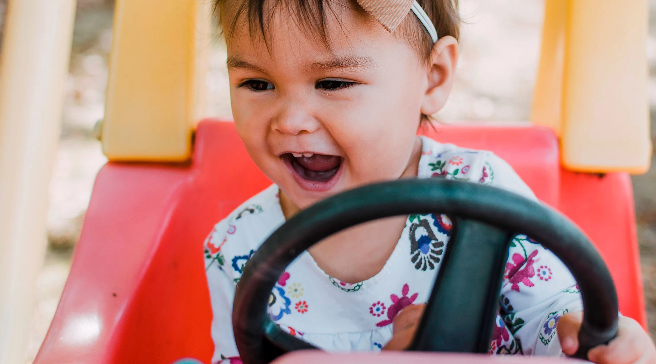 toddler happily playing in red kid car