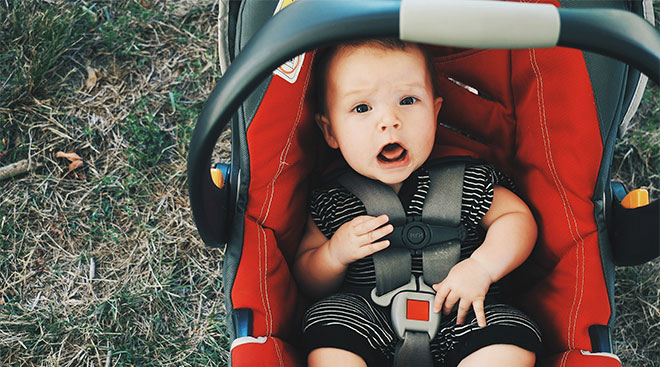 baby strapped in car seat and looking at the camera with an open mouth