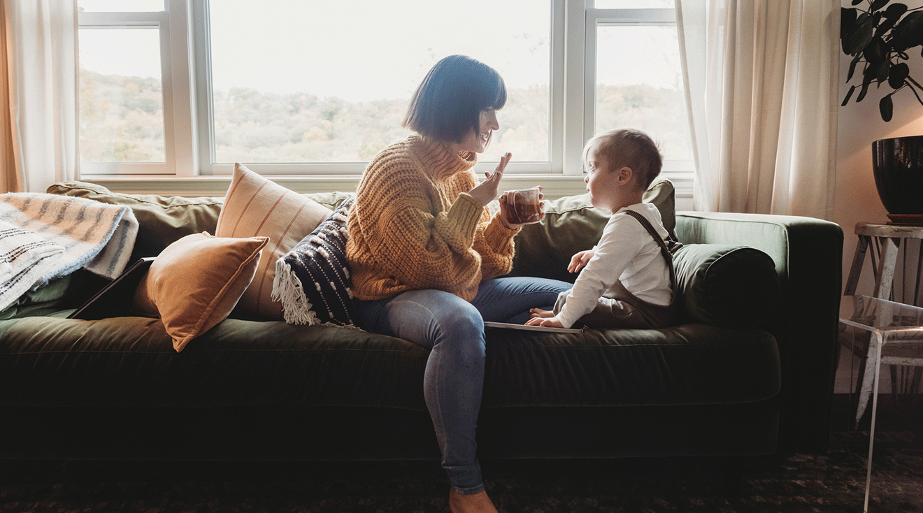 mother teaching toddler sign language while sitting on couch at home