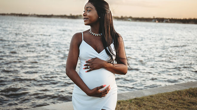 pregnant woman smiling in front of a background of water