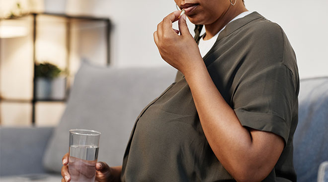 close up of pregnant woman taking a vitamin with water