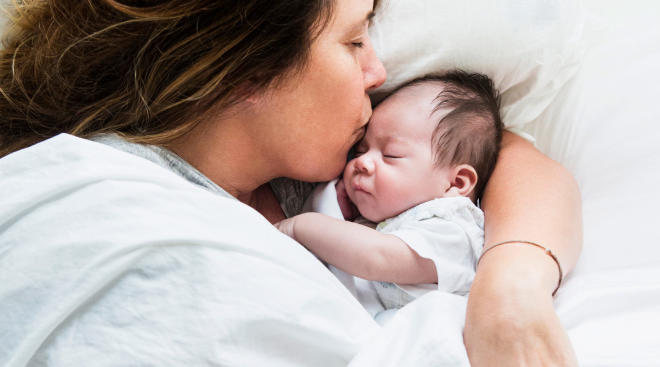 new mom sweetly kissing her newborn baby in bed