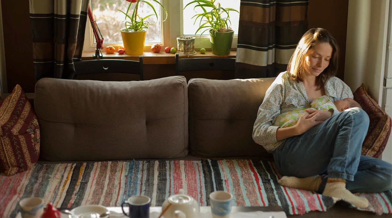 mother holding newborn baby while sitting on couch at home