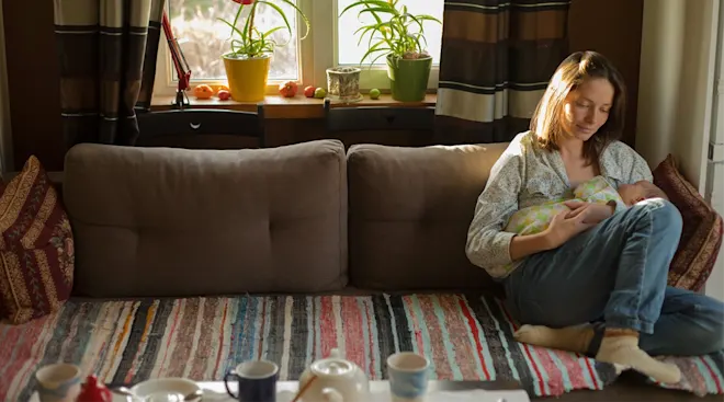 mother holding newborn baby while sitting on couch at home