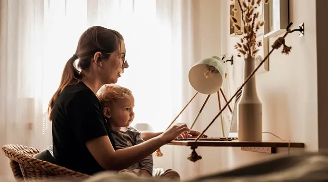 mother and baby sitting at desk working at home during covid pandemic