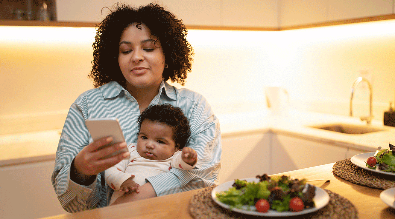 mother looking at phone while holding baby at home