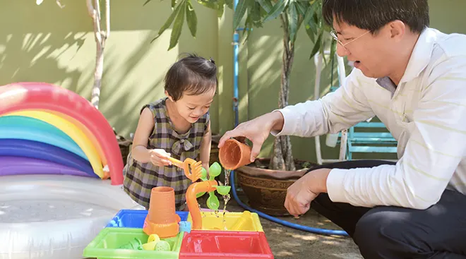 toddler girl and her father playing with water table toy outside
