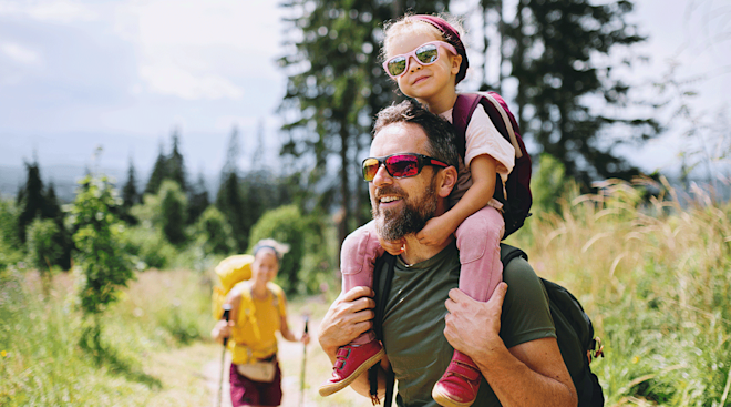 dad carrying daughter with sunglasses on while hiking outside
