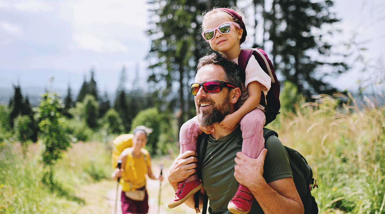 dad carrying daughter with sunglasses on while hiking outside