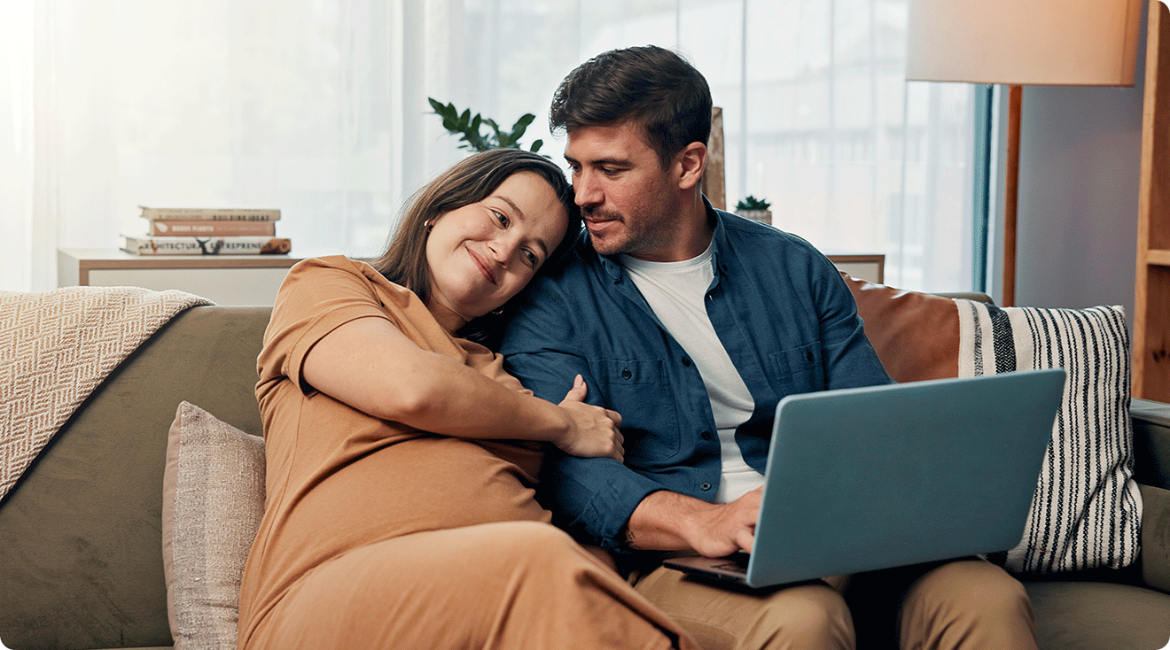 pregnant couple looking at laptop at home on the couch choosing a baby name