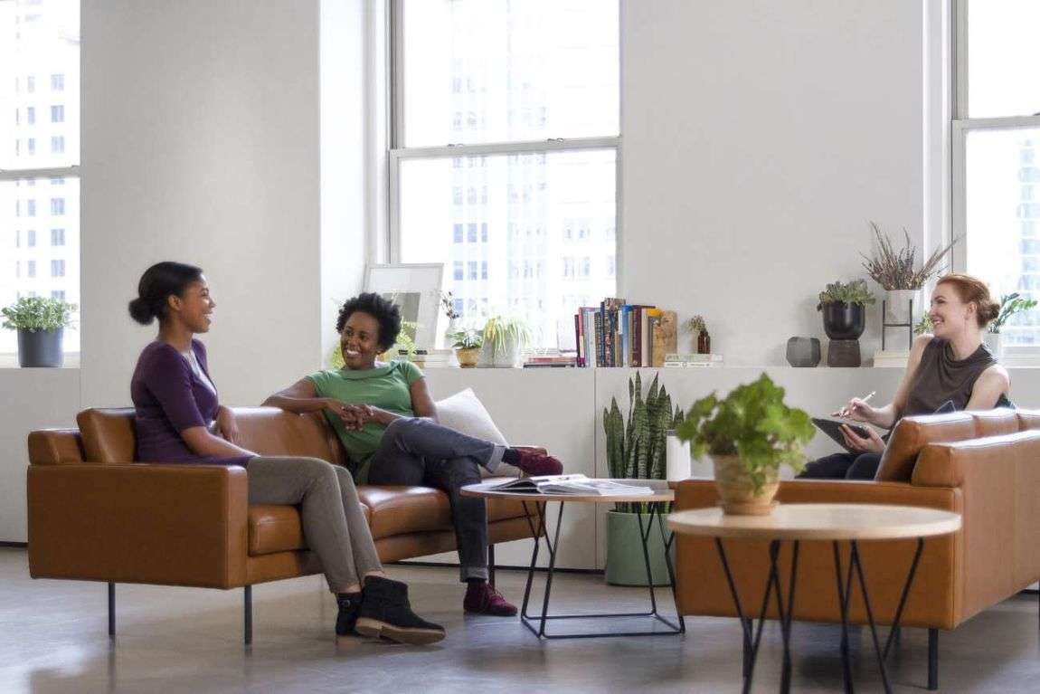 Three women sitting on couch surrounding by plants.