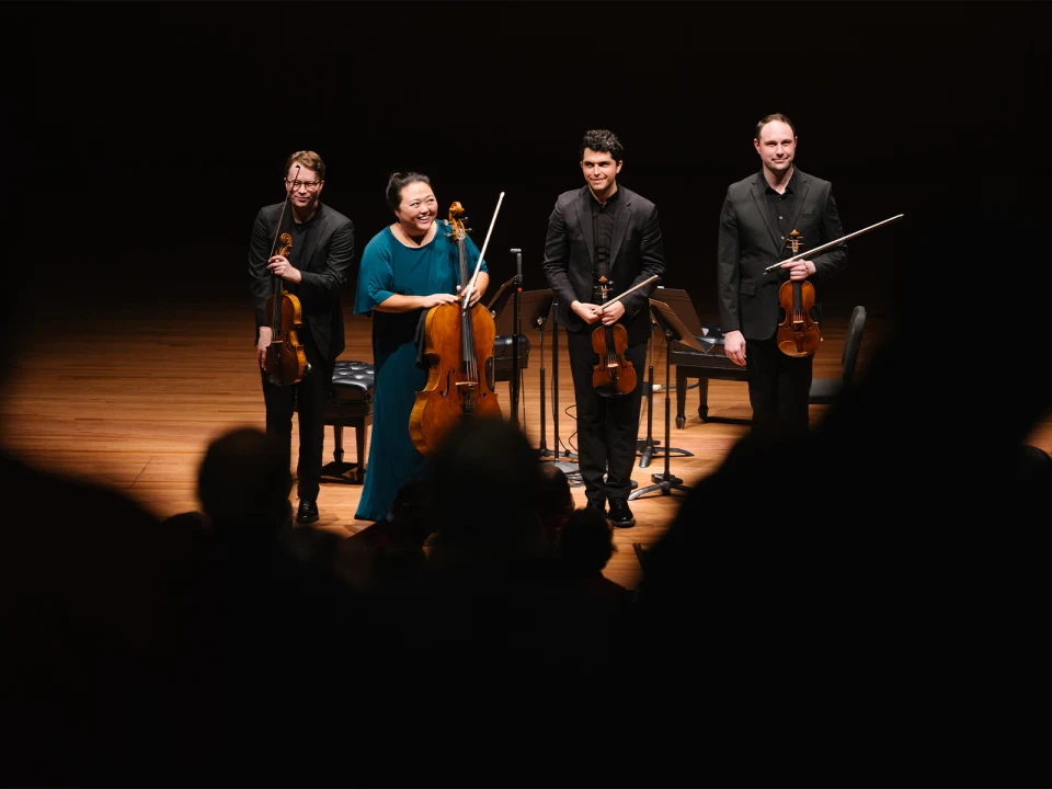 A string quartet on stage acknowledges the audience's applause after a performance.