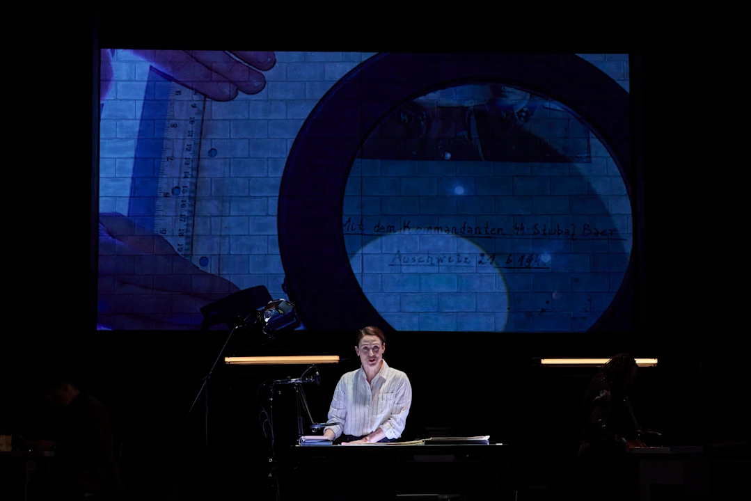 Person sitting at a desk with a large projected image of a document in the background, featuring hands holding a magnifying glass and ruler.