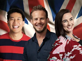 Three people smiling and standing in front of a large, unfurled British flag.