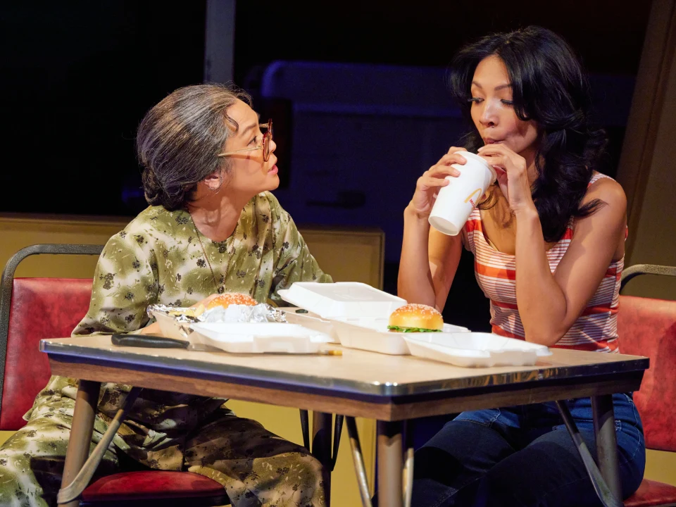 Older woman watching a younger woman sip her soda at the table.
