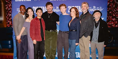 Eight cast members of The Fantasticks pose for a group photo in front of a blue branded backdrop.