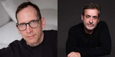 Two men sit separately; the man on the left wears glasses and a dark shirt, while the man on the right has gray hair, a beard, and a black shirt, both facing the camera.