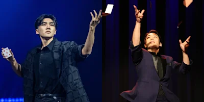 Two magicians performing card tricks on stage, one holding a playing card and the other tossing cards into the air.