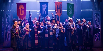 A group of people in robes and scarves stand on stage smiling, holding four colorful banners labeled G, R, H, and S.
