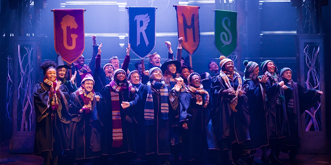 A group of people in robes and scarves stand on stage smiling, holding four colorful banners labeled G, R, H, and S.