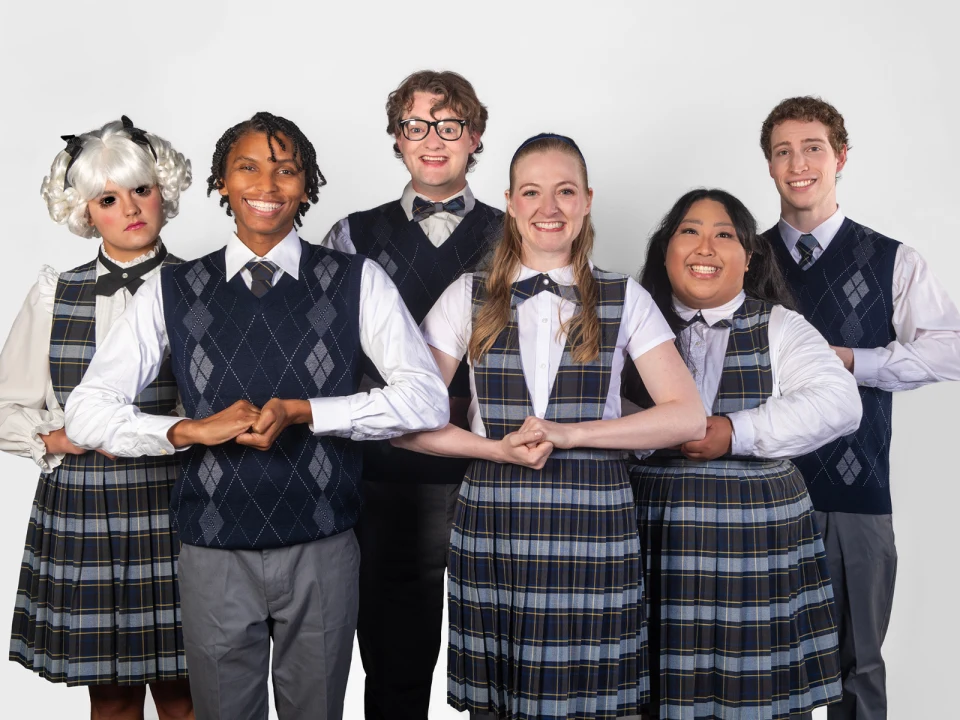 Production shot of Ride the Cyclone in San Francisco, showing ensemble wearing school uniforms stand in a line, holding each other's arms.