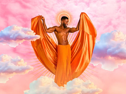 A smiling shirtless man stands with arms raised, holding orange fabric like wings, surrounded by clouds and a golden halo on a pink sky background.