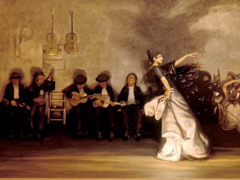 A flamenco dancer performs in front of five seated musicians, some playing guitars, with two guitars hanging on the wall behind them.