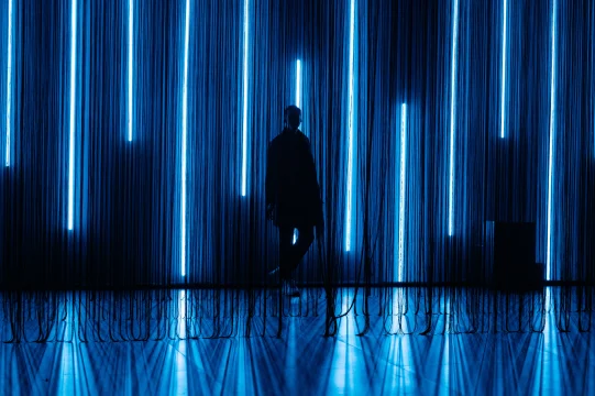 Silhouette of a person standing in front of vertical blue neon lights against a dark background.