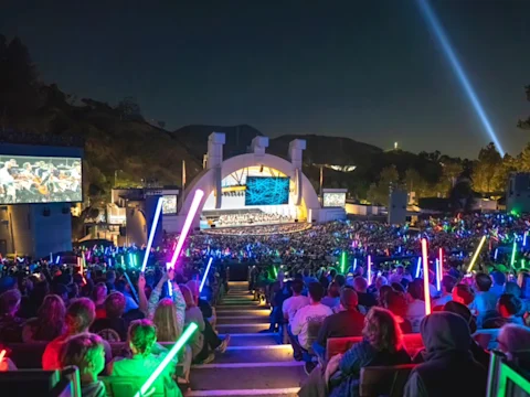 Photo of Hollywood Bowl amphitheater with a large crowd attending a nighttime event and colorful lightsabers.