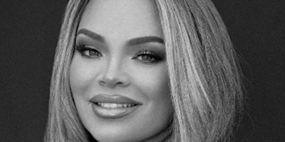 A person with long, straight hair and makeup smiles while looking at the camera in this black and white portrait.
