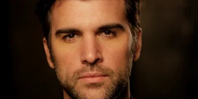 Close-up portrait of a man with dark hair and a light beard looking directly at the camera.