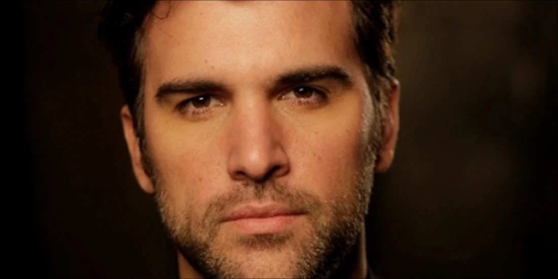 Close-up portrait of a man with dark hair and a light beard looking directly at the camera.