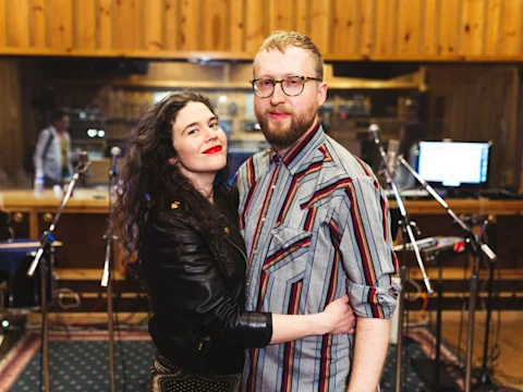 A woman and man posing together in a recording studio.