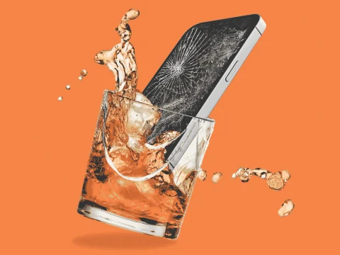 A smartphone with a cracked screen is partly submerged in a glass of liquid, splashing the contents. The orange background highlights the contrast.