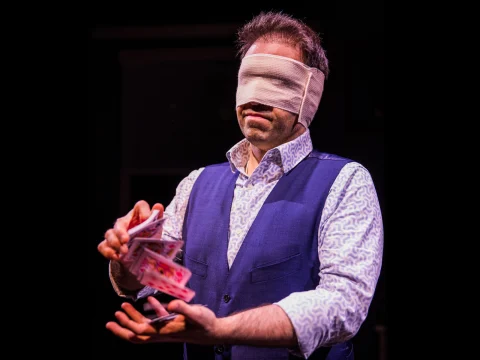 Production photo of The Hope Theory in Los Angeles, California with the performer Helder Guimarães with a white blindfold and performing a card trick.