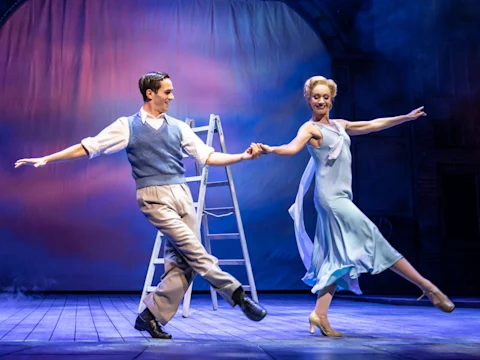 Don Lockwood and Kathy Seldon embrace under a red umbrella in the rain in Singin' in the Rain