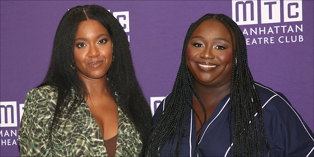 Two women stand together in front of a purple Manhattan Theatre Club backdrop, one wearing a green patterned blazer, the other a navy blue outfit with white trim.