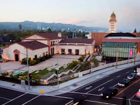 Aerial view of a civic building complex with a clock tower, modern and historic architecture, and surrounding roads with cars in Beverly Hills, California.
