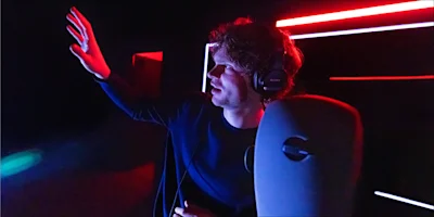 A person wearing headphones reaches their hand out toward a glowing red light in a dark room.